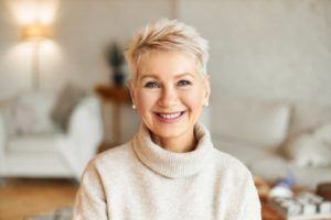 an older woman wearing a sweater and smiling, showing off her new dental implants in Tysons